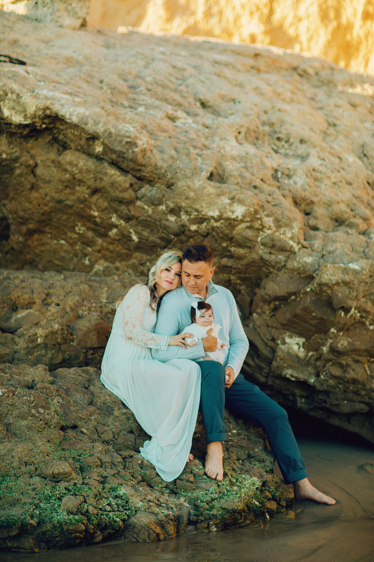 Family Portrait Photo Of Couple  Holding Their Baby While Seated On a Rock Los Angeles