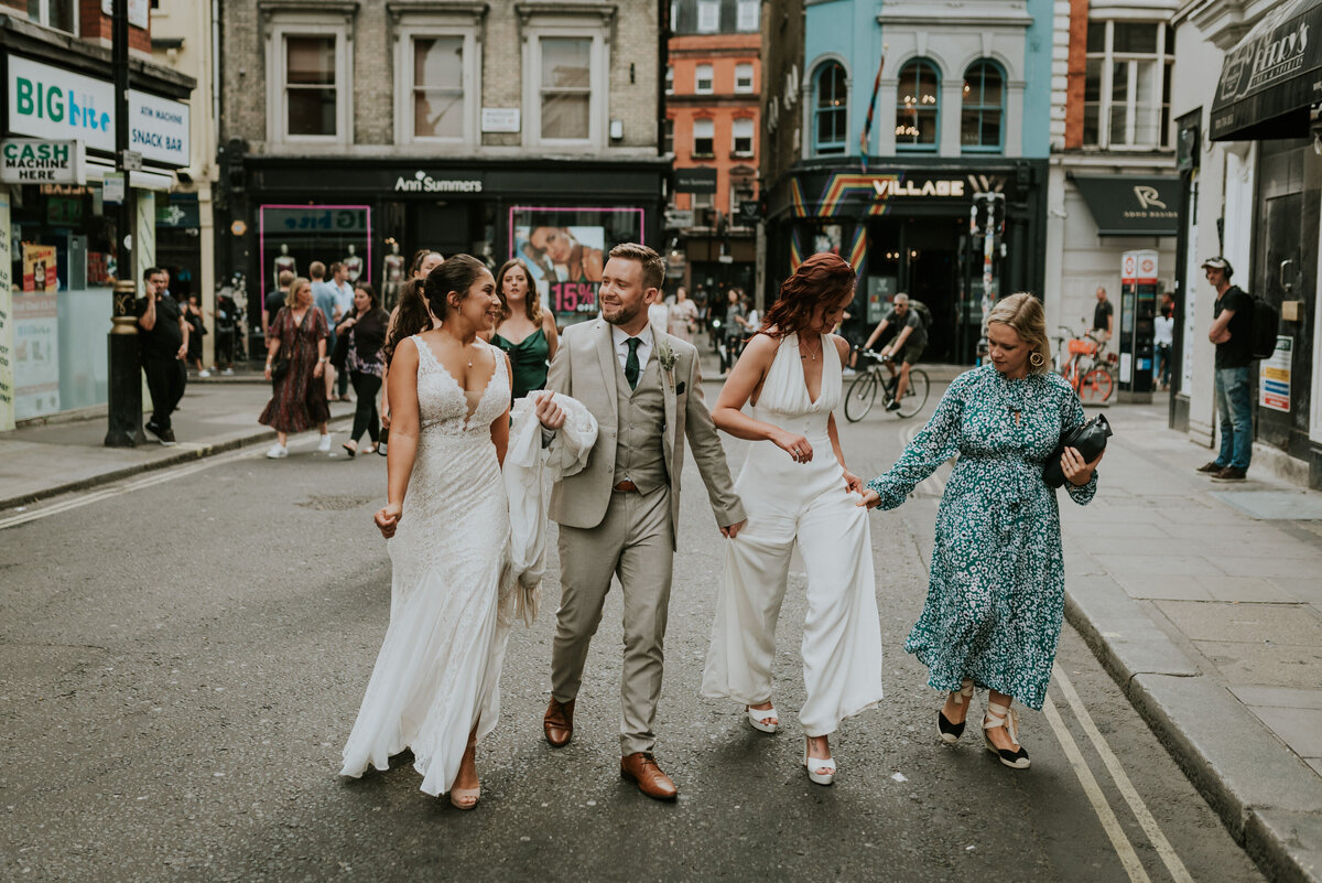 Two brides and bridesmaids walking through Soho