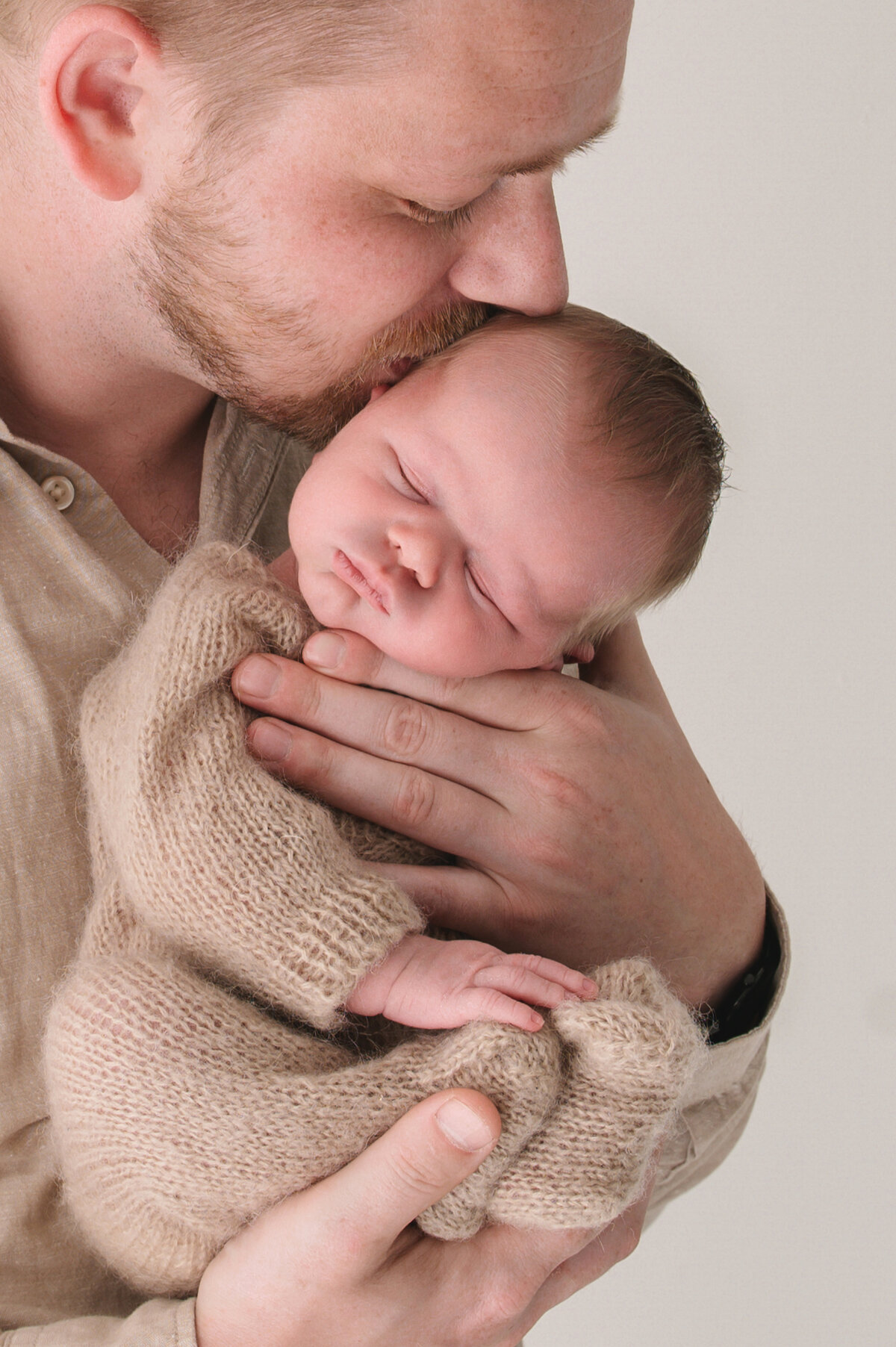 kersverse papa die zijn pasgeboren zoontje een kus geeft in een neutrale beige setting