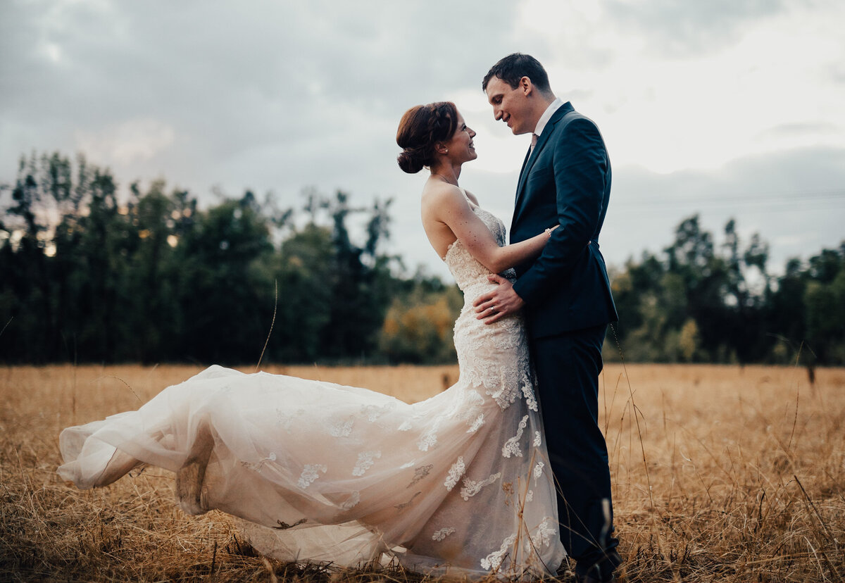 Groom holds bride in a field while her dress flows in the wind