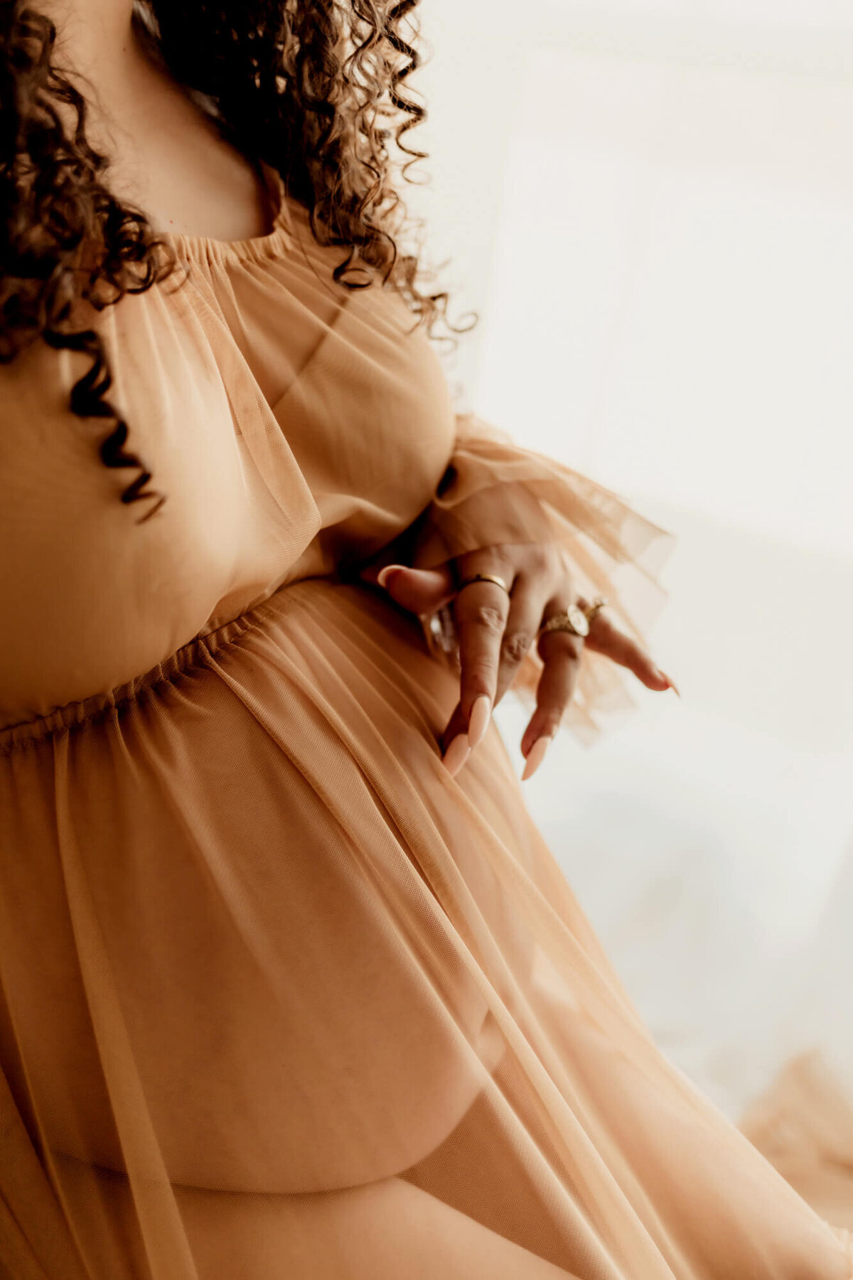 Pregnant woman with curly hair traces her belly in Yukon, Oklahooma.