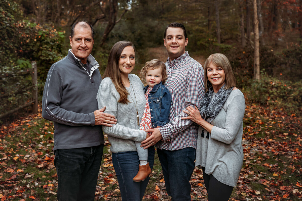 multi generational family smiling for their fall family portrait with trees behind them