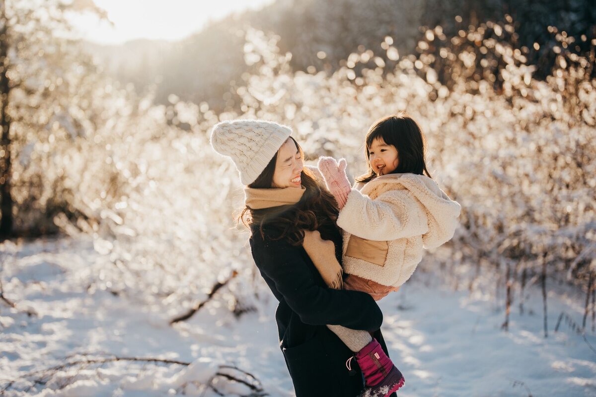 mom-holding-her-daughter-playing-in-snow