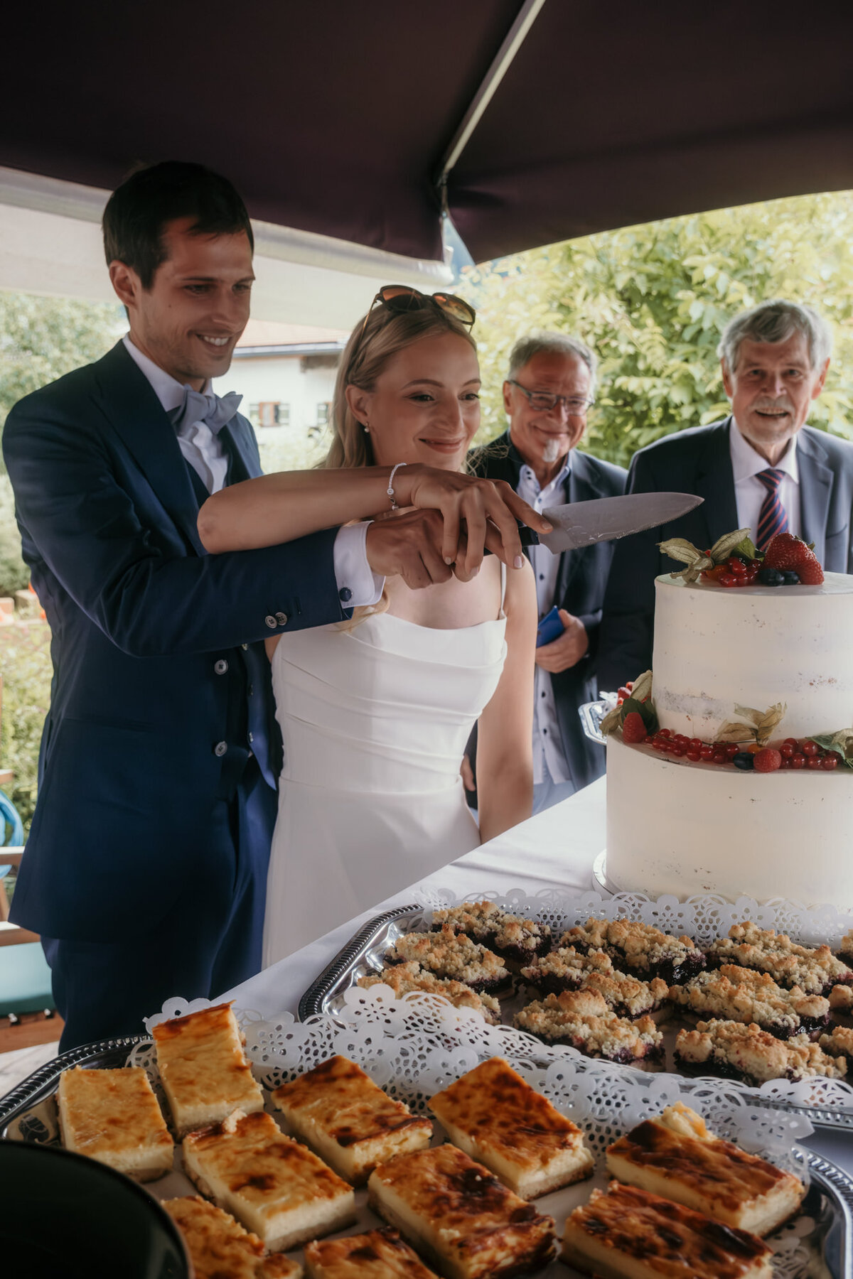 The bride has her hand on top while they cut their wedding cake.