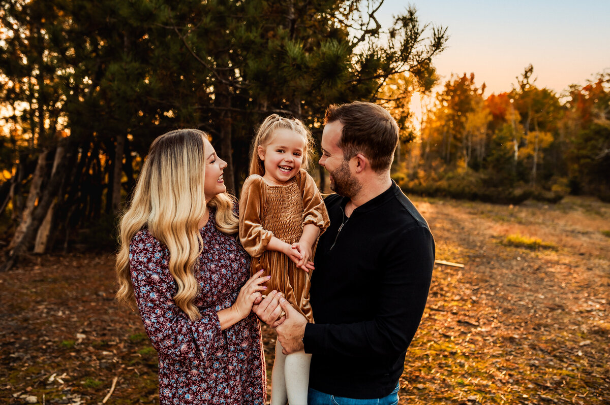 Family laughing together during Ottawa fall mini session with golden autumn leaves in the background.