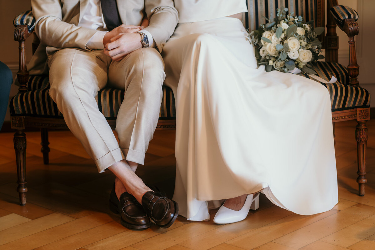 The wedding couple sits next to each other on a bench. Photography of their lower halves.