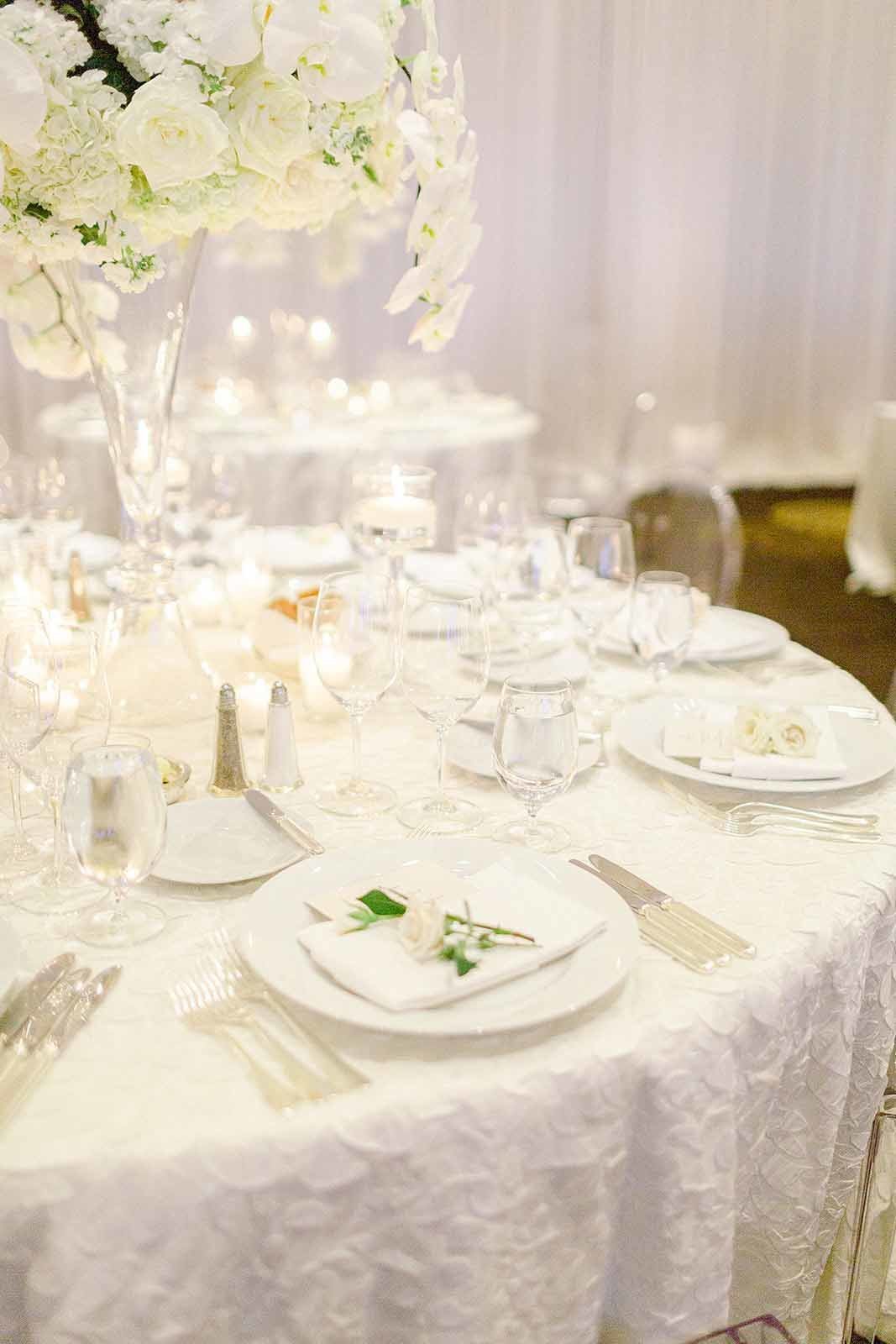 dinner table with white table linen, white flower centerpiece, candles, and draped walls