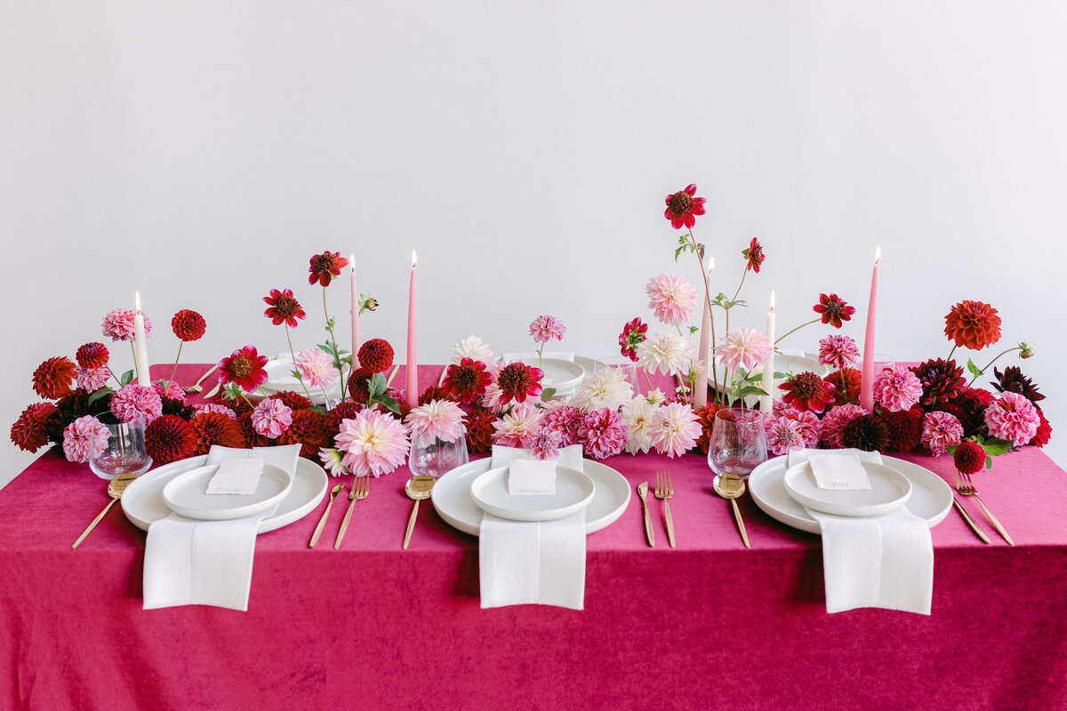 A centrepiece of bold pink and red flowers on a table with a bright tablecloth.