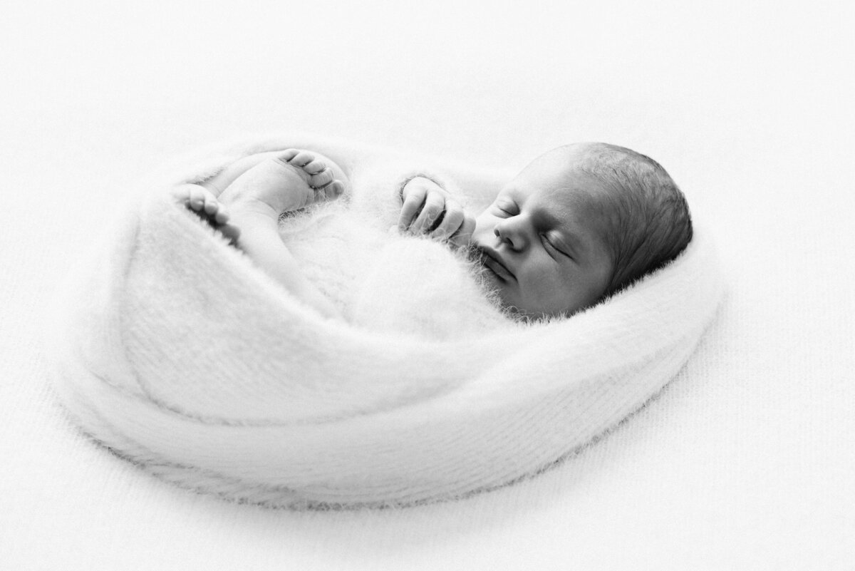 A newborn girl all wrapped up in a white blanket sleeping during a photoshoot in Billingshurst