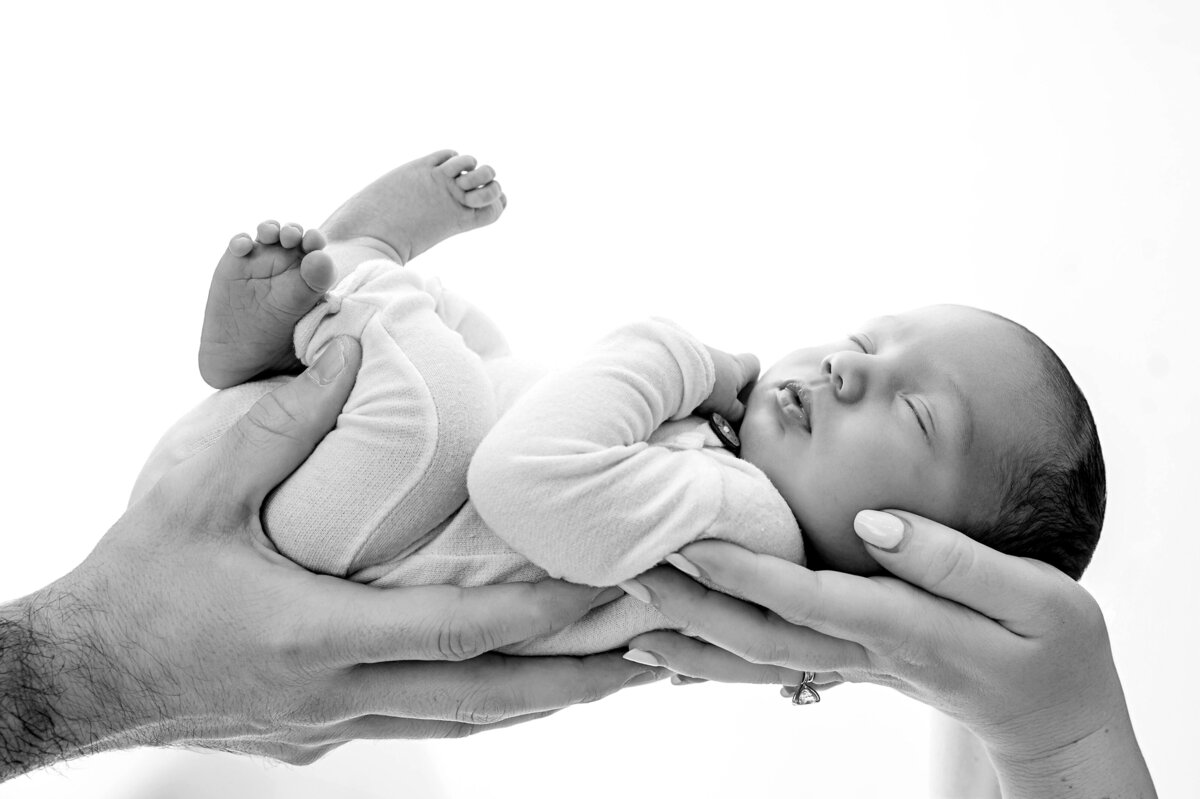 mom and dad hands holding a newborn baby sweetly in black and white