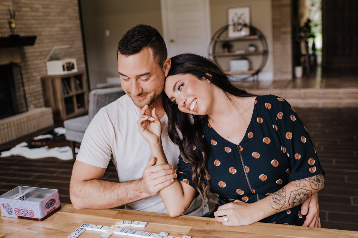 Couples Photography, at a table in the living room, a woman leans into her partner as they play dominoes