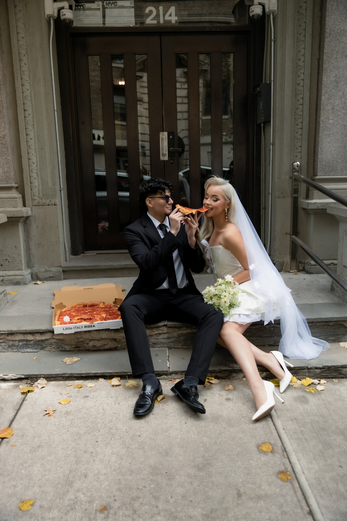 Bride and groom sharing a romantic moment while splitting a slice of pizza in NYC.