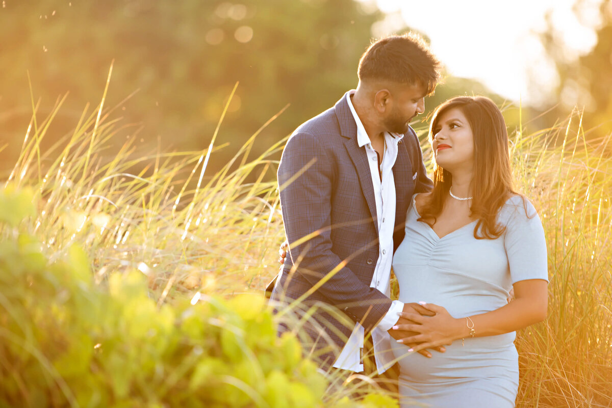 husband and wife cradling mom's pregnant belly for her outdoor beach maternity photography session in Burlington, On in the golden hour