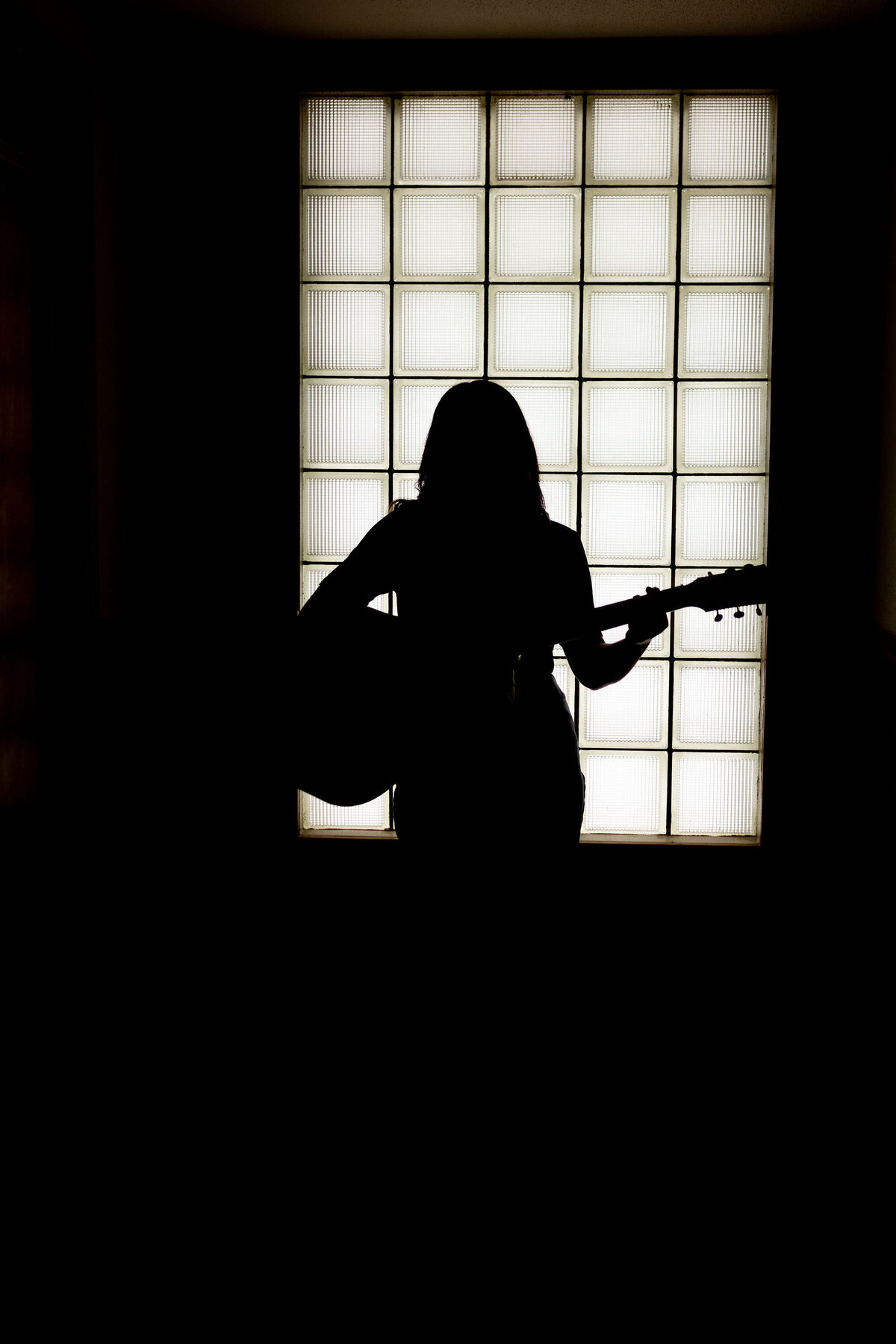 silhouette portrait of girl with guitar standing in front of window