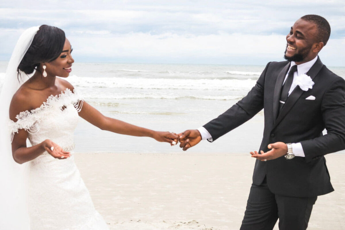 Bride and groom holding hands and facing each other smiling on the seaside