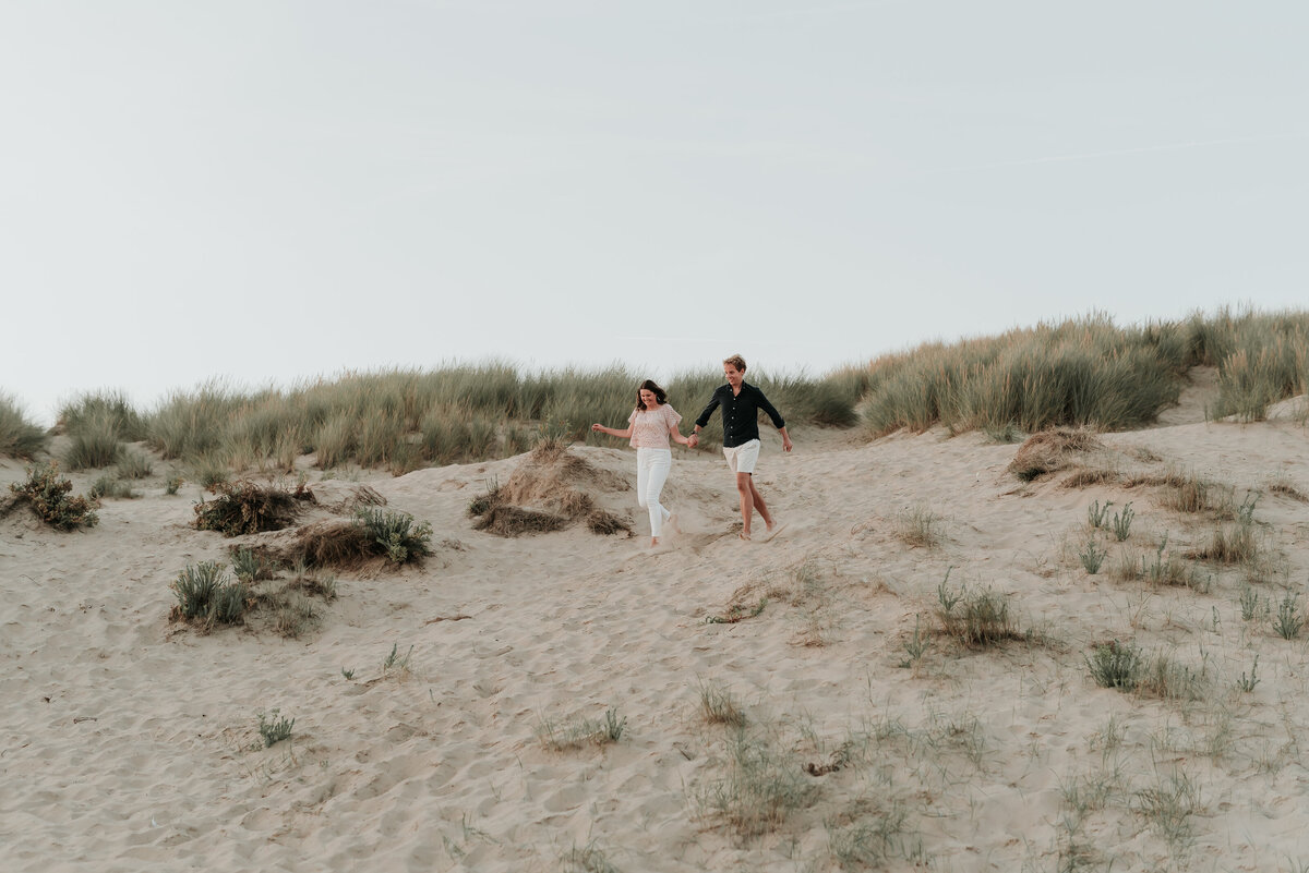 Couple running hand in hand down sand dune at Camber Sands beach