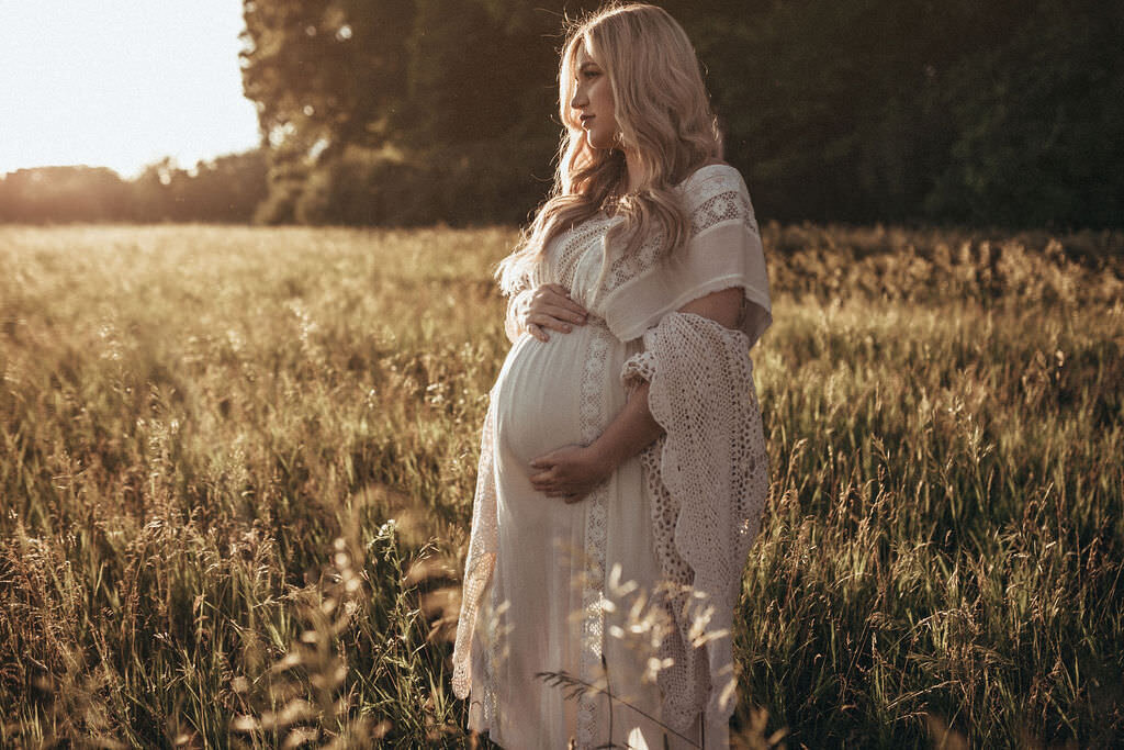 pregnant woman holding belly in field