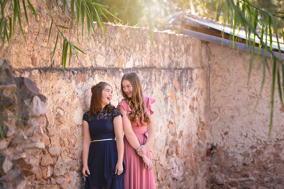 Prom pictures with two senior girls in formal dresses posing next to a stone wall captured by senior picture photographers near me