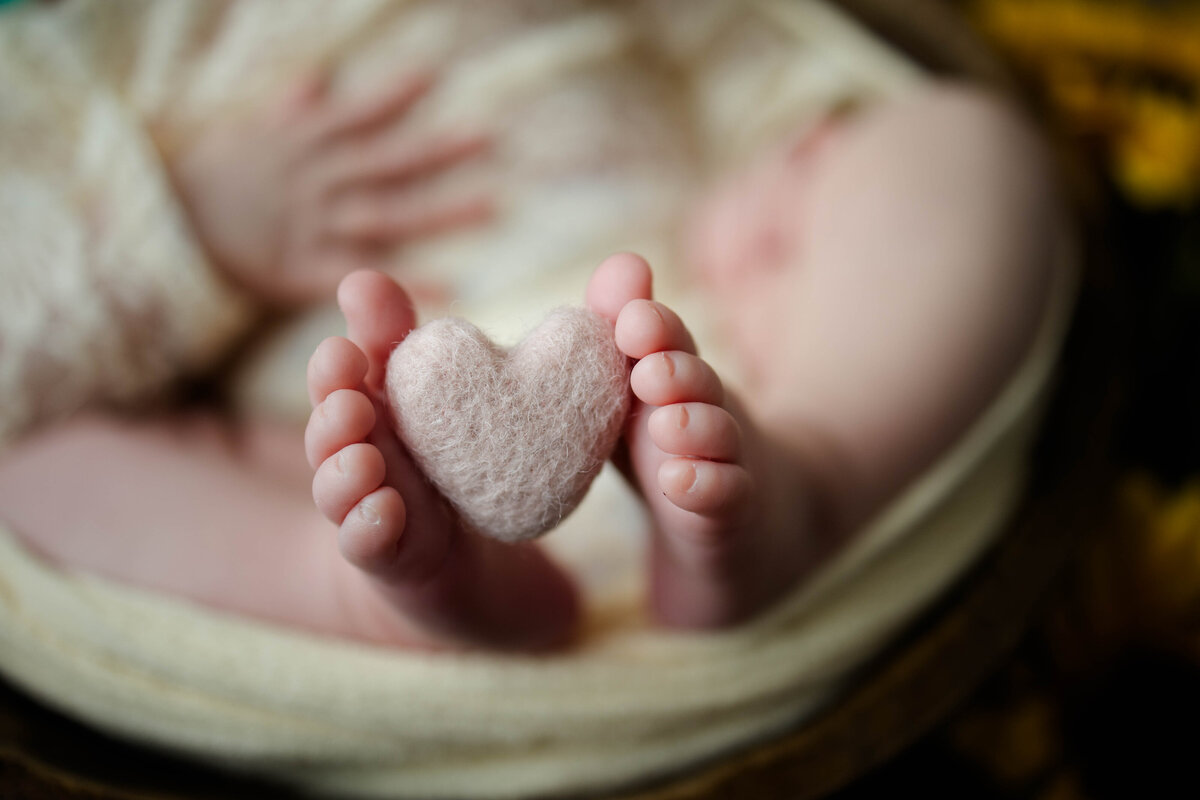 Newborn baby girl with a fluffy heart tucked between her toes