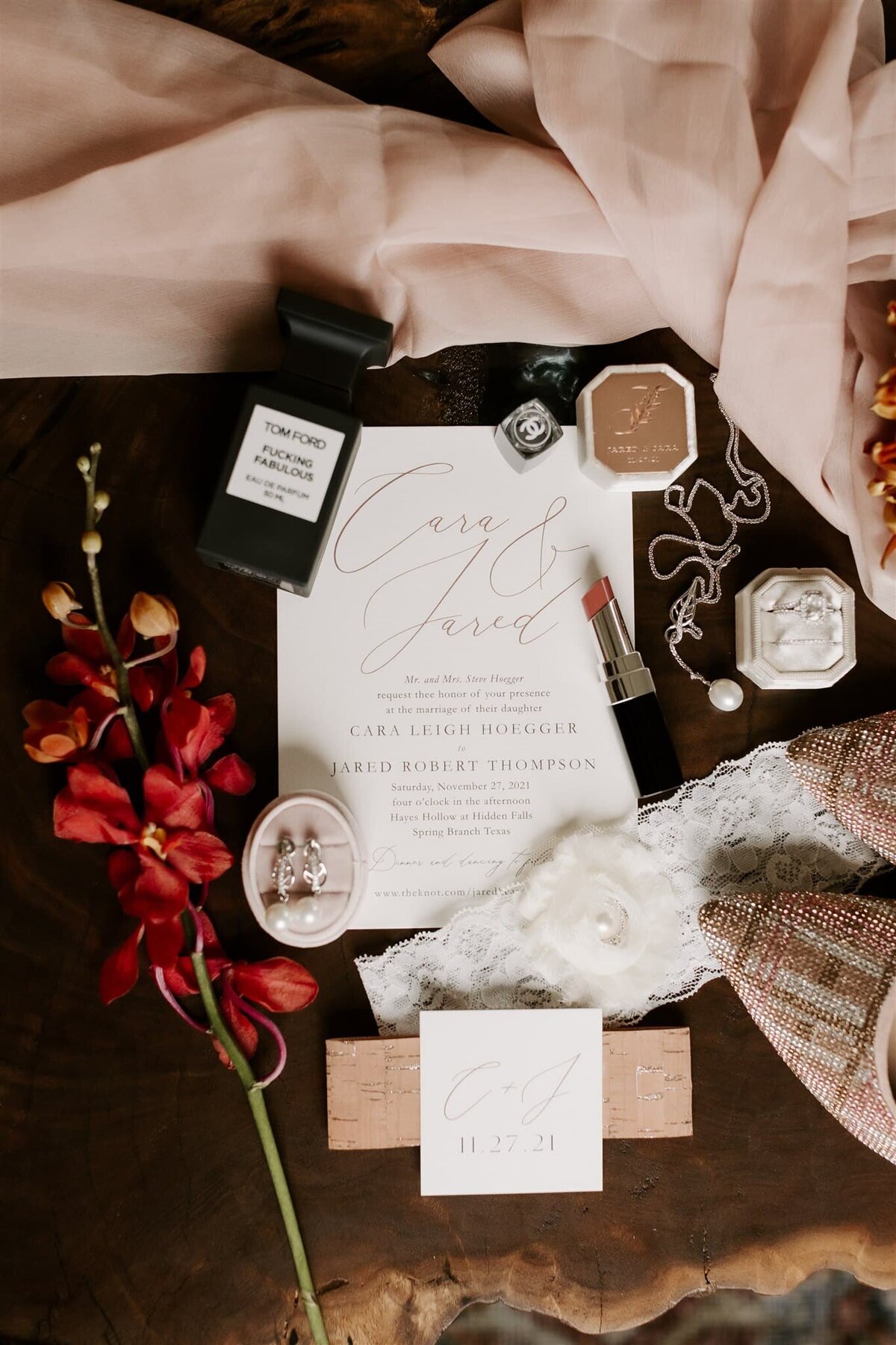 wedding flat lay including perfume, dark lipstick, lace garter, and tweed heels