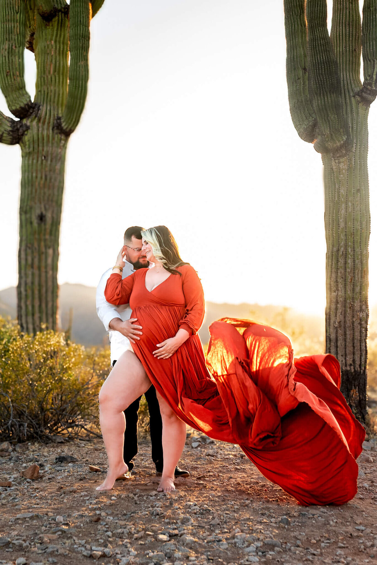 husband with mom-to-be in fiery dress train tossed in the air. Photographed by Cactus & Pine Photography