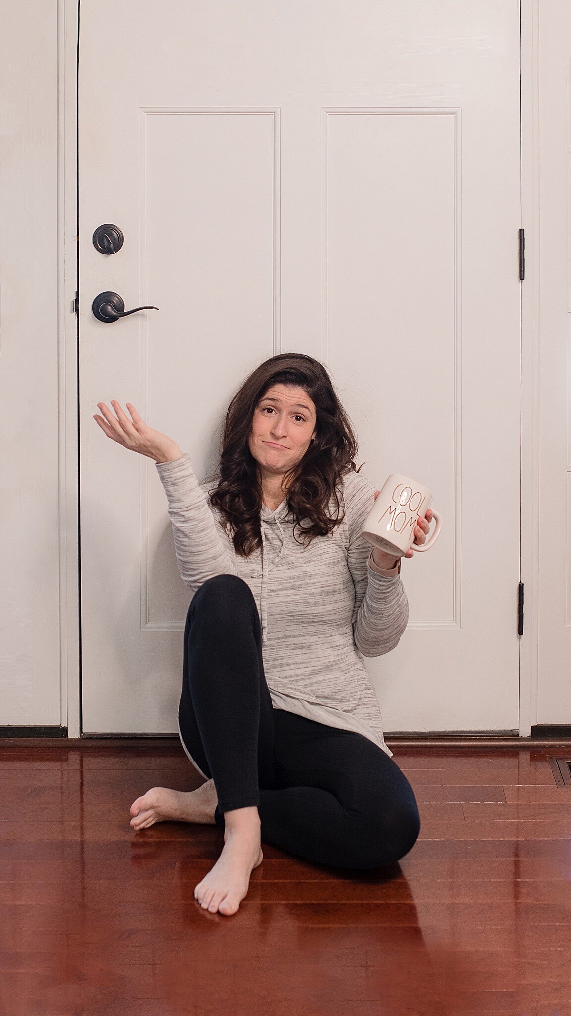 mom sitting on floor holding coffee mug and shrugging