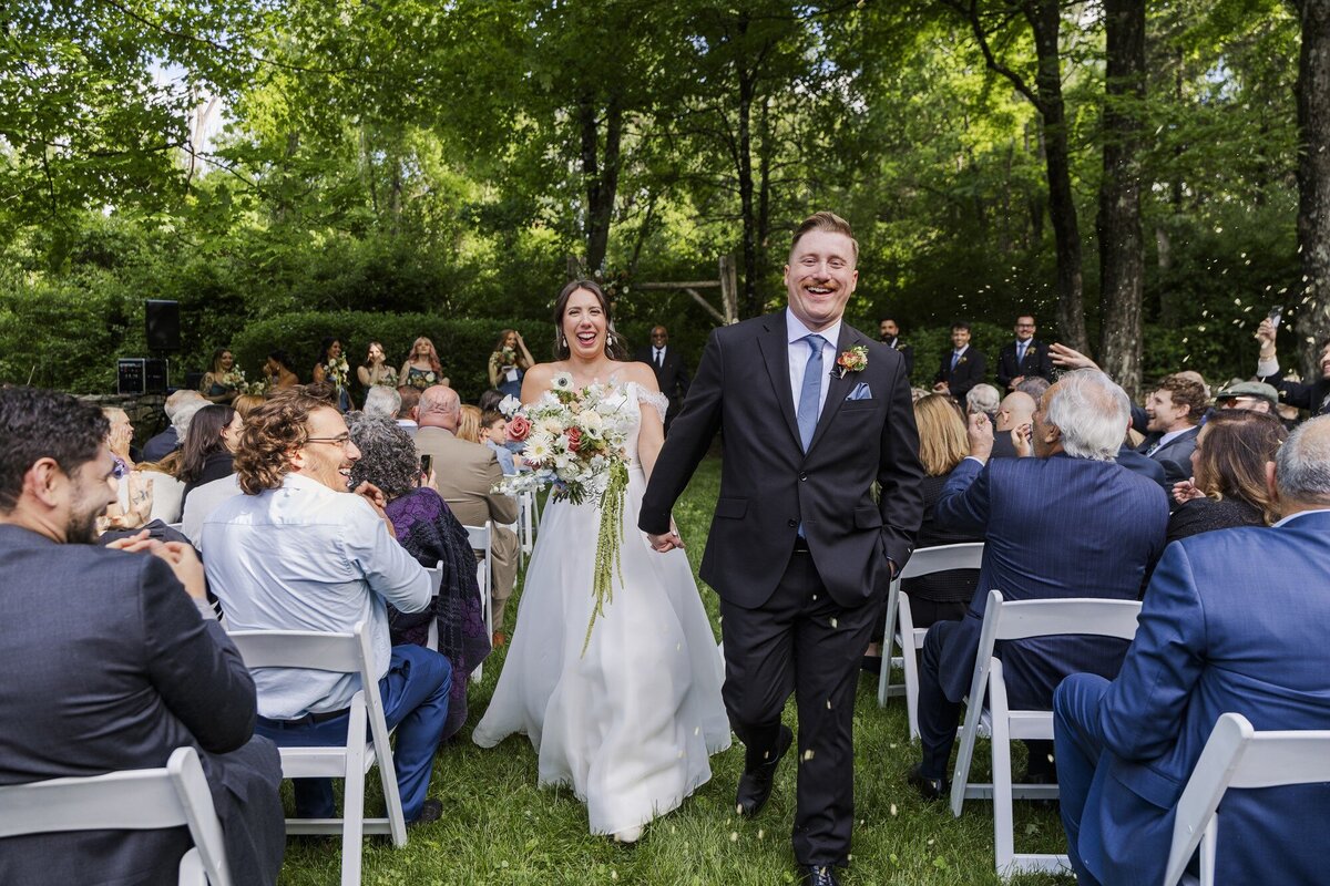 Bride and groom walking up the aisle between smiling guests at an outdoor wedding ceremony