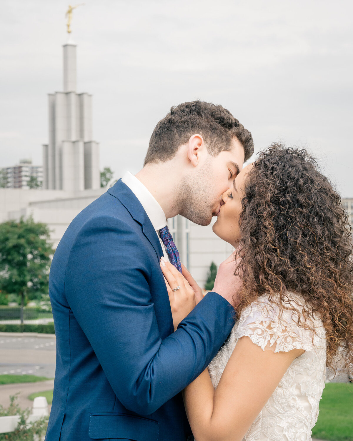 A bride and groom stand kissing gently in front of The Hague Netherlands Temple for the Church of Jesus Christ of Latter-Day Saints in Zoetermeer, Netherlands