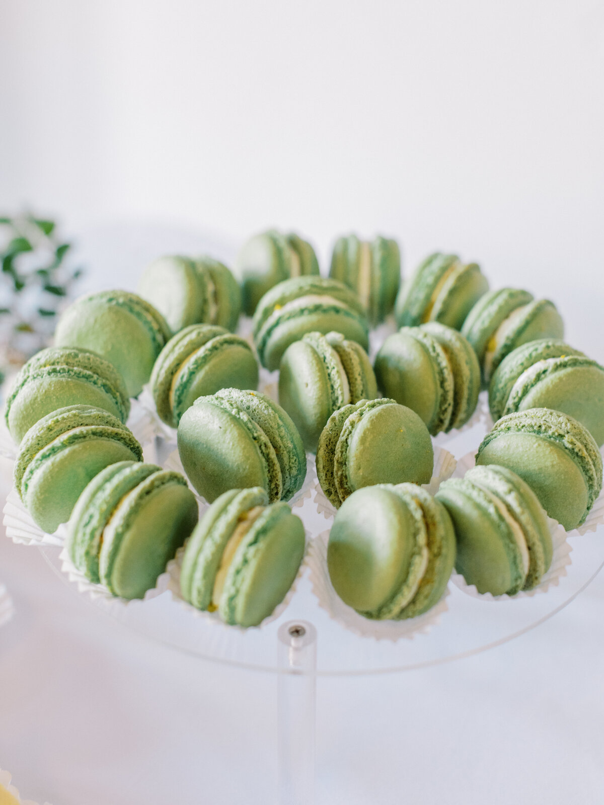 Green French macarons displayed on a clear acrylic stand as part of the wedding dessert table.