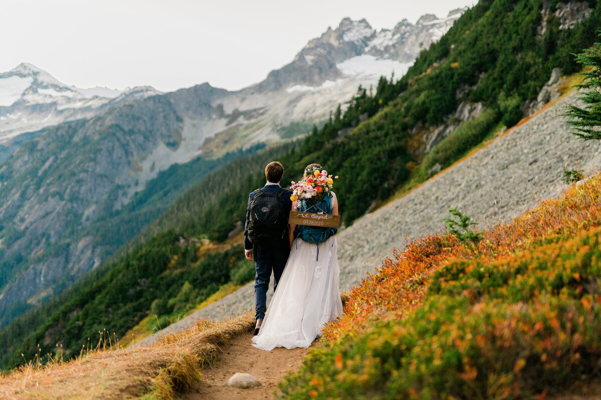 Bride & groom walking along Cascade Pass trail with "Just Married" sign on backpack! 