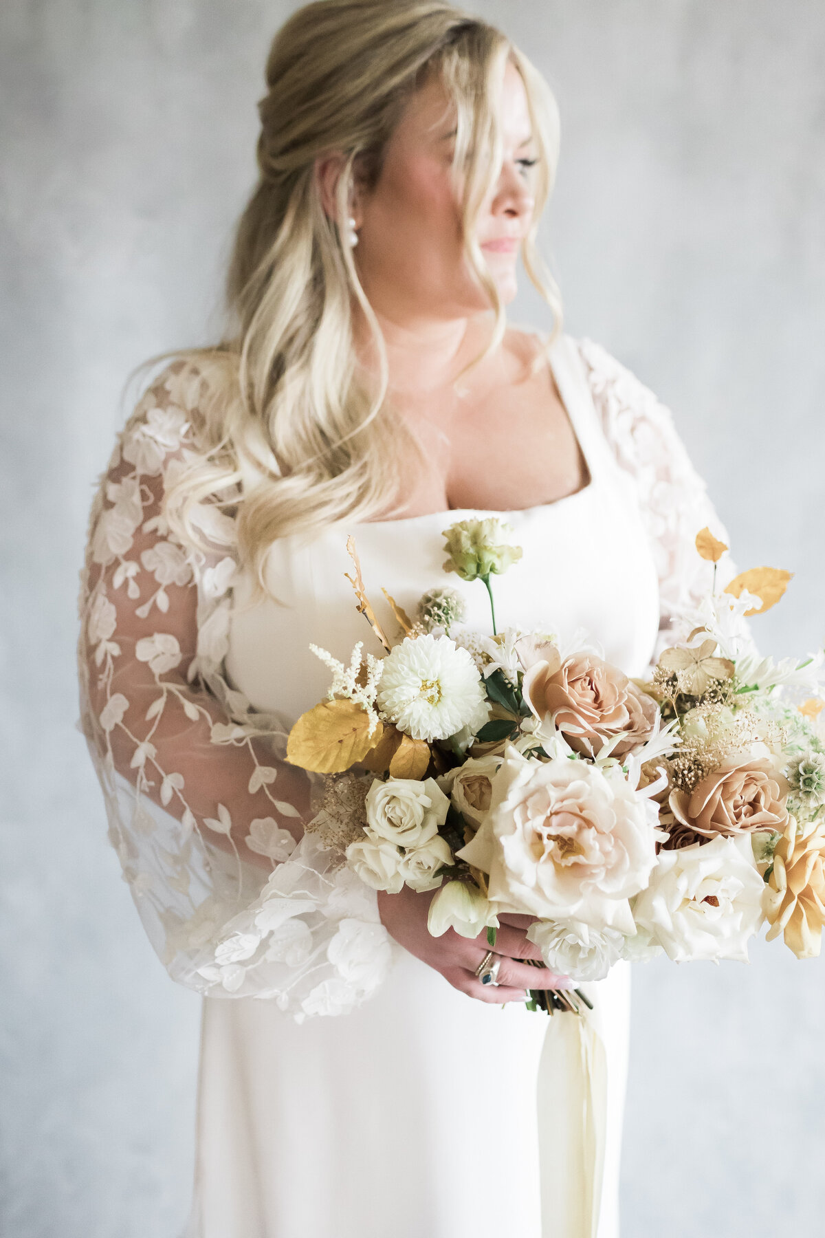 Stunning bride in wedding gown with lace sleeves holds her bouquet