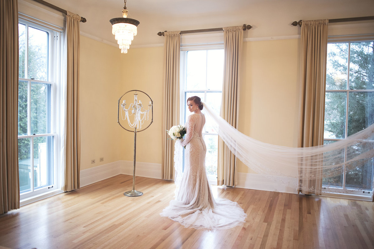 A woman in a white dress is standing in natural light. Her veil is long