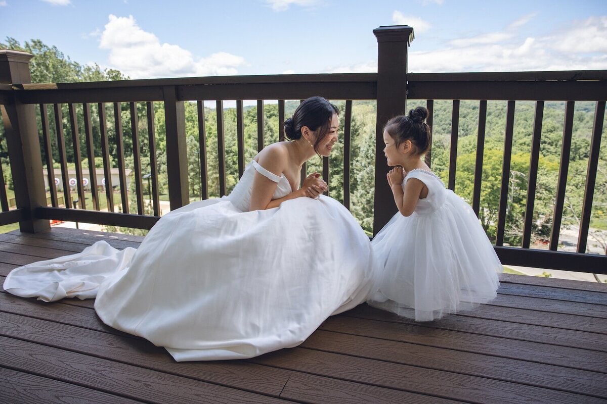 Bride holding flower girl and laughing on sunny balcony