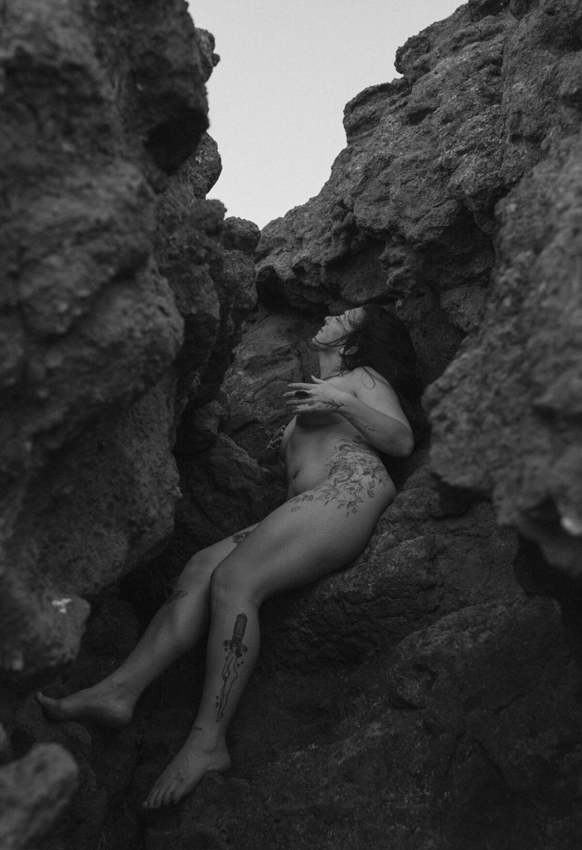 nude female with tattoos lays against the Moab, Utah desert rocks on a warm day