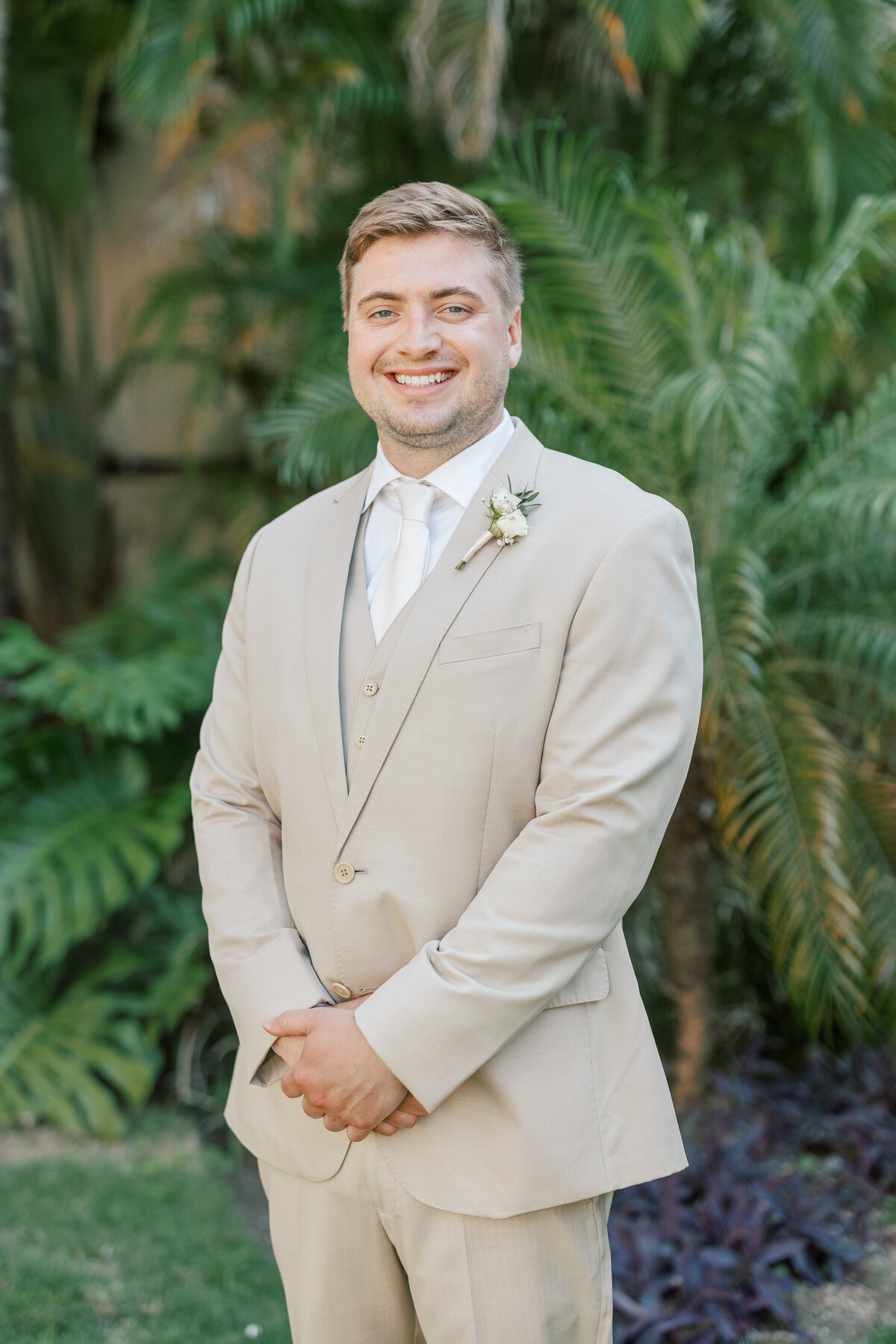 Groom smiles in tan suit with tropical greenery in the background at Cancun wedding.