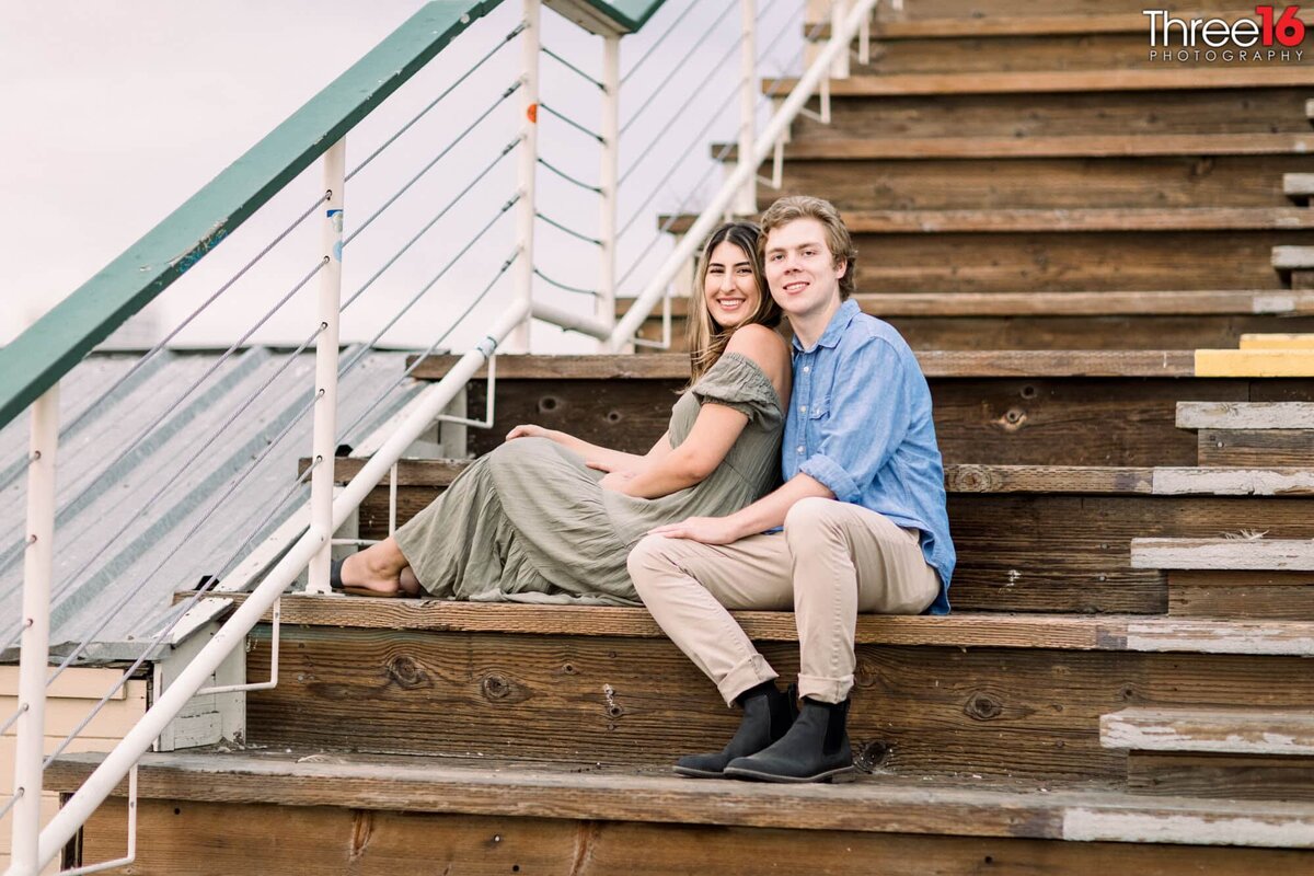 Engaged couple cozy up together on the stairs as they pose for photos