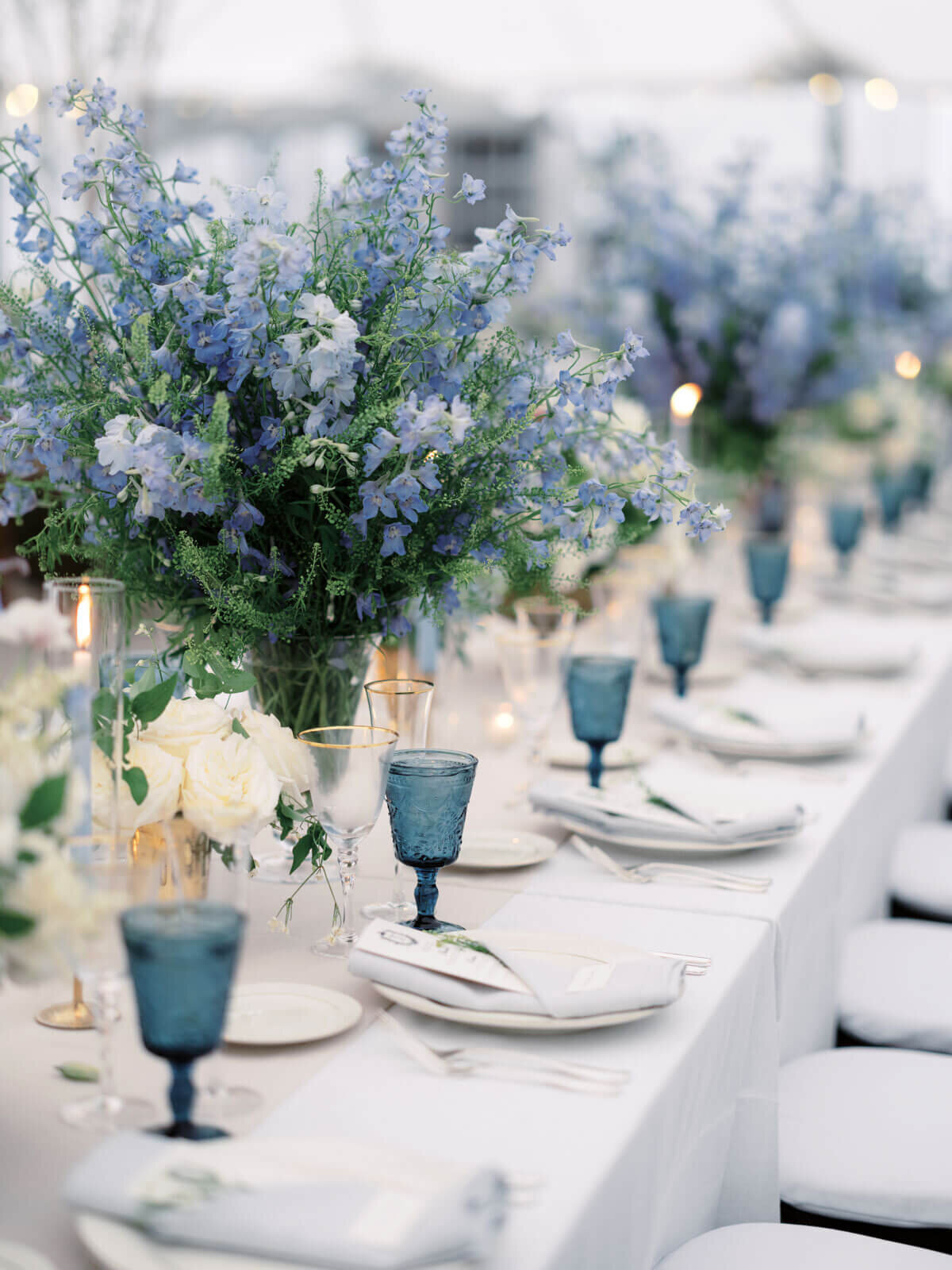 An elegant wedding dining table with pretty blue flower centerpieces and wine glasses at The Lion Rock Farm, CT. Image by Jenny Fu Studio