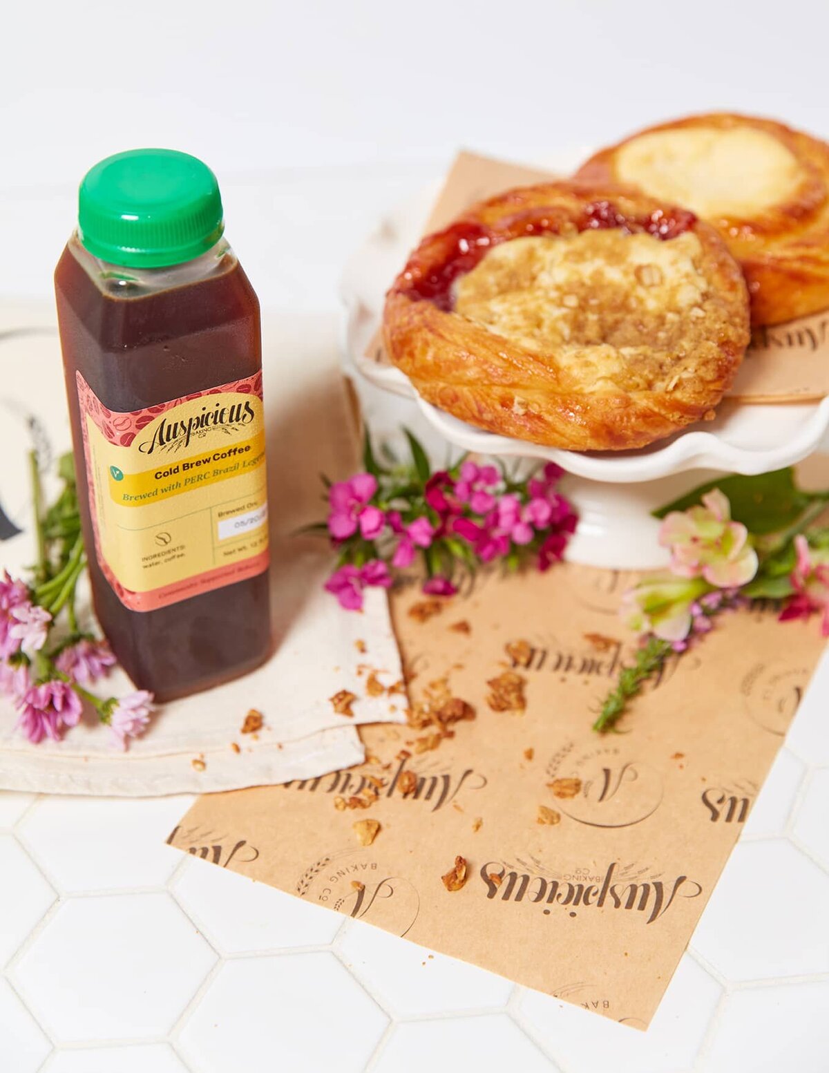 A plastic bottle of cold brew coffee sits next to a deli sheet and pastries