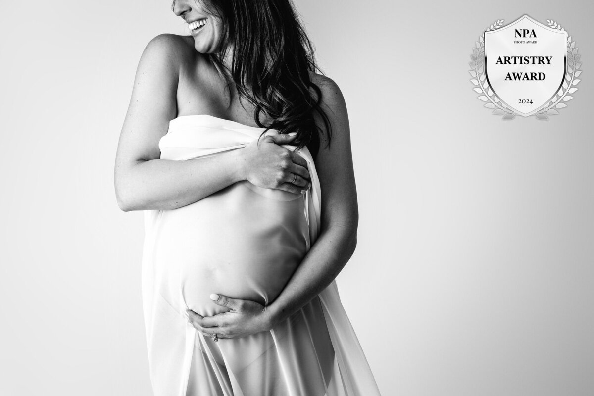 mother cradling her baby bump draped in fabric in east jordan studio