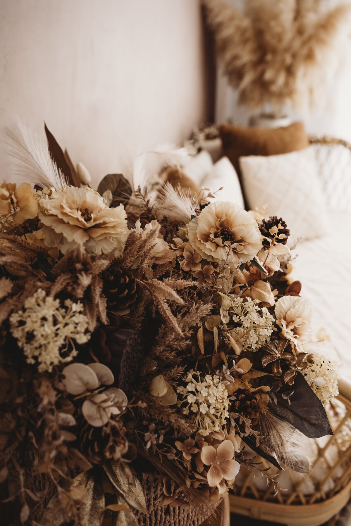 A close-up of a bouquet with dried flowers in neutral tones, including beige and brown, placed near a wicker chair with white cushions and a pampas grass arrangement in the background. Perfect for capturing the serene ambiance of Wollongong motherhood sessions by an NSW family photographer.