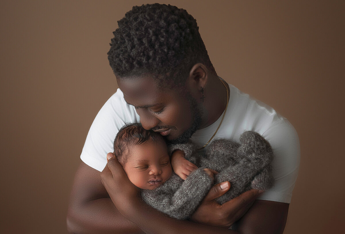 New dad holds his baby boy for newborn photoshoot. Baby is held high in dad's arms and is smelling the top of baby's head. Dad's eyes are closed and smiling. Captured by Bryn Mwar Philadelphia and Main Line photographer Liza Nicole.