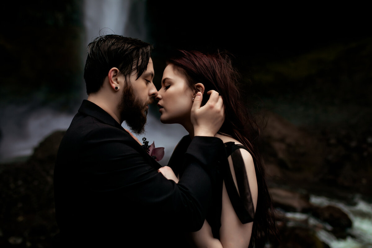 A couple sharing an intimate moment in front of a waterfall, captured by an Oregon Coast Elopement and Wedding Photographer.