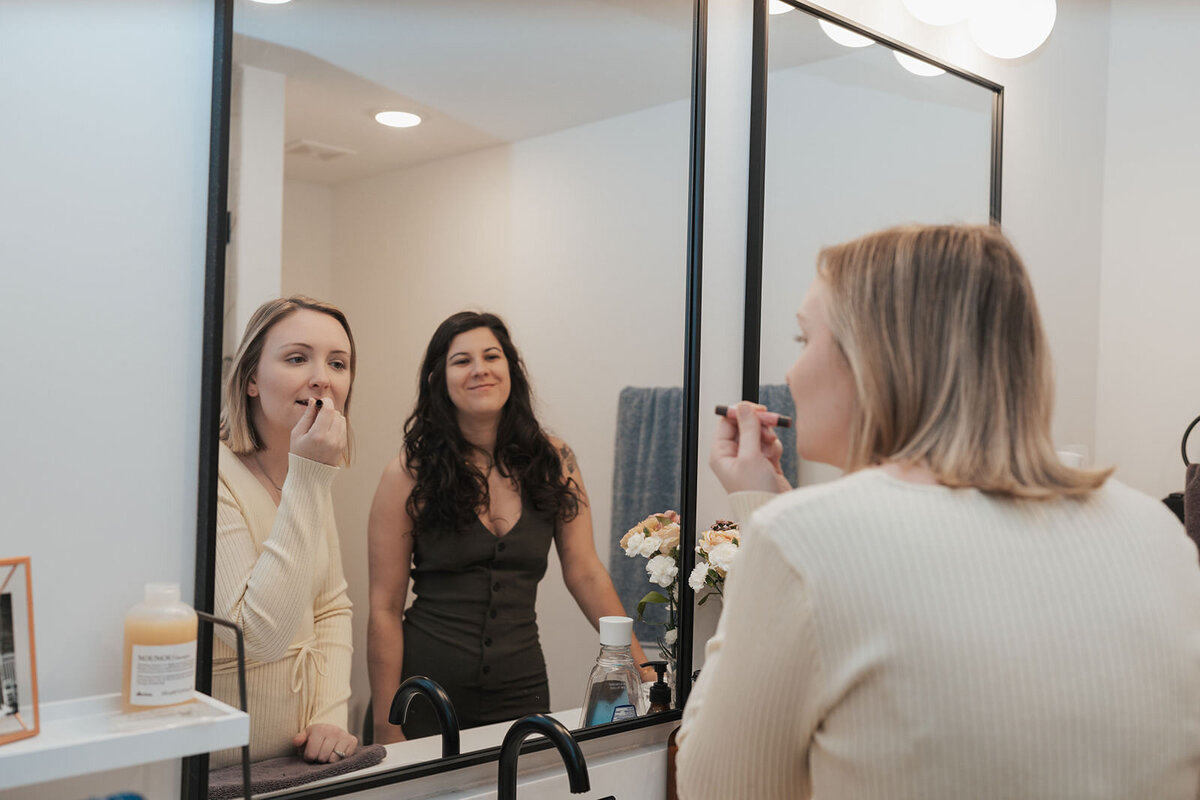 Women look in mirror as one wife applies her lipstick