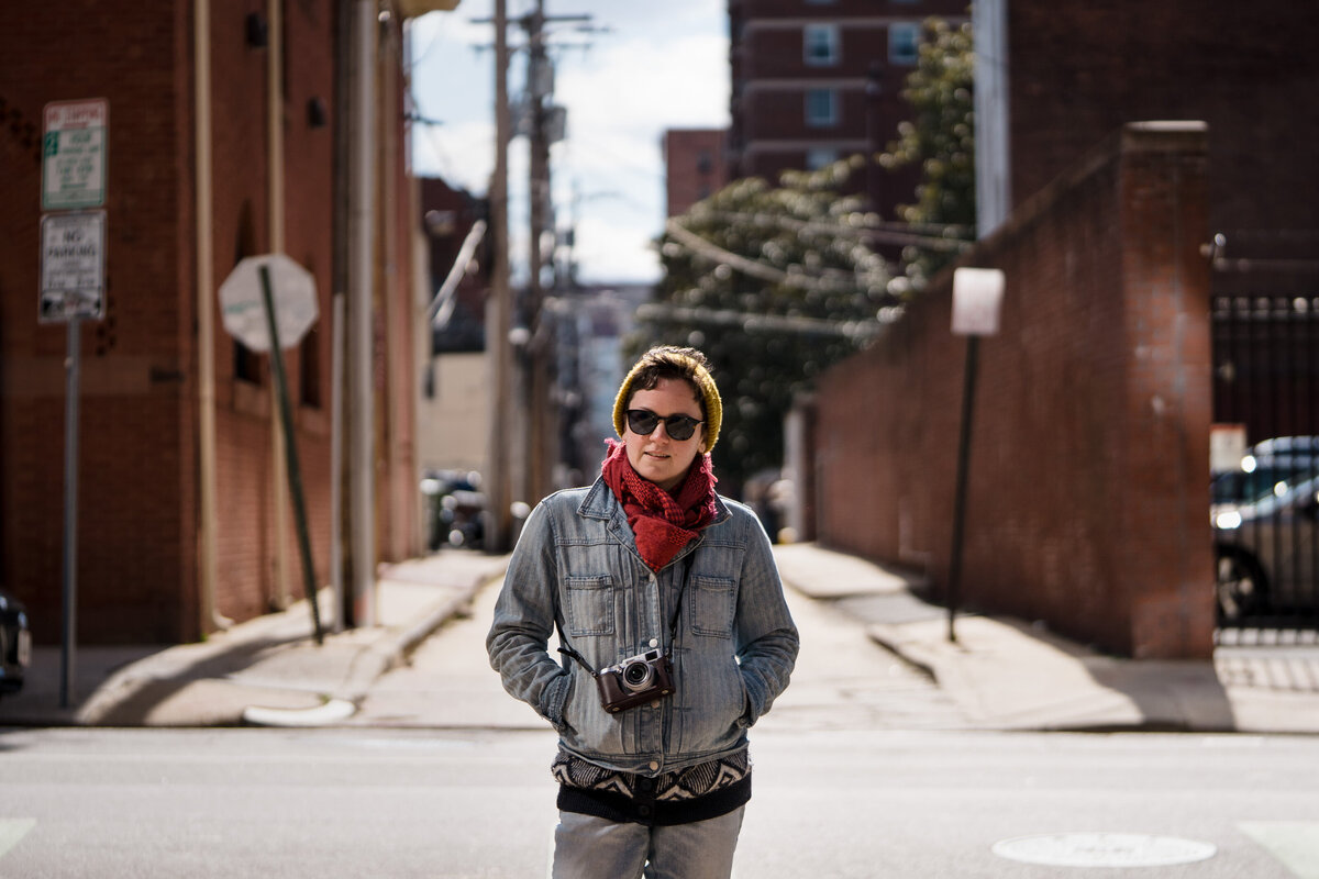 A person standing in front of a city street with a camera around their neck.