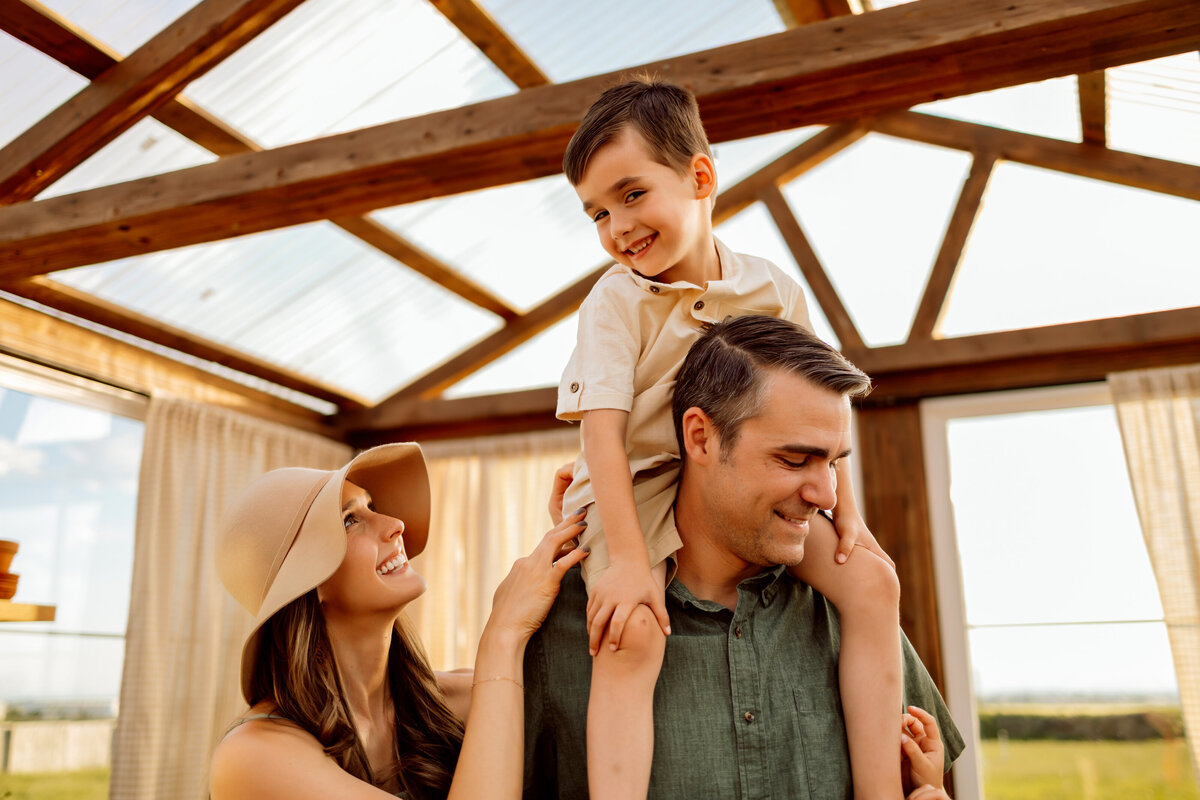 Little boy sits on dads shoulders in a greenhouse for their family photos shoot in Denver