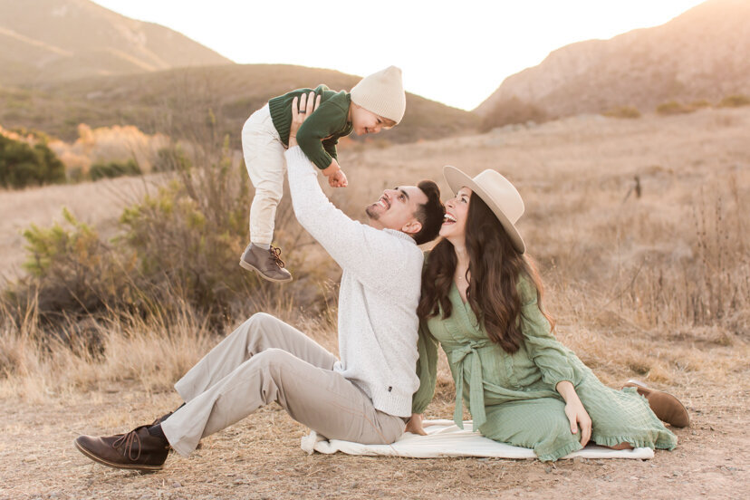 parents-sitting-in-field-holding-up-son-mission-trails-san-diego-portrait