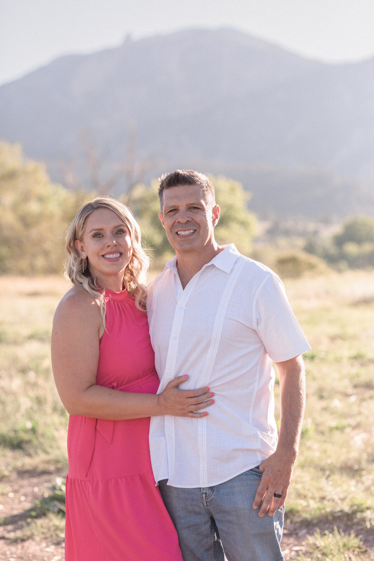 A woman in a bright pink dress poses with her fiance' at South Mesa Trail, a great Boulder engagement photography location