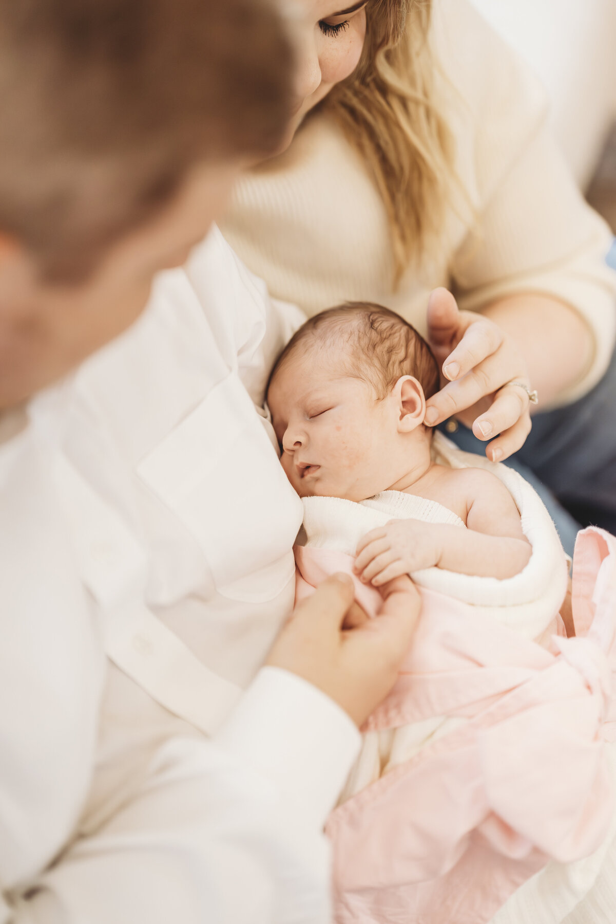 Warm-toned portrait of parents holding their baby in a blush wrap during an in-home Kansas City newborn session.
