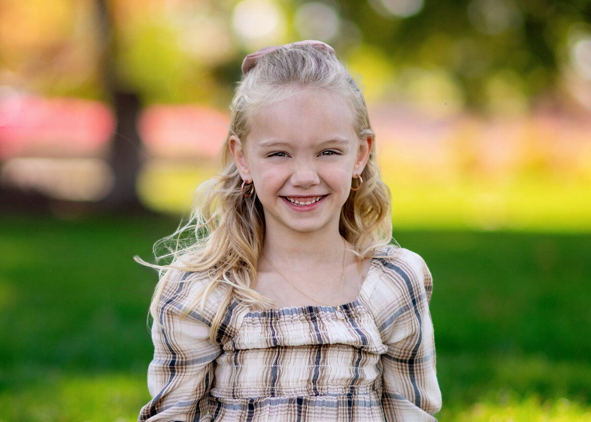 Girl smiles with trees and greenery behind her