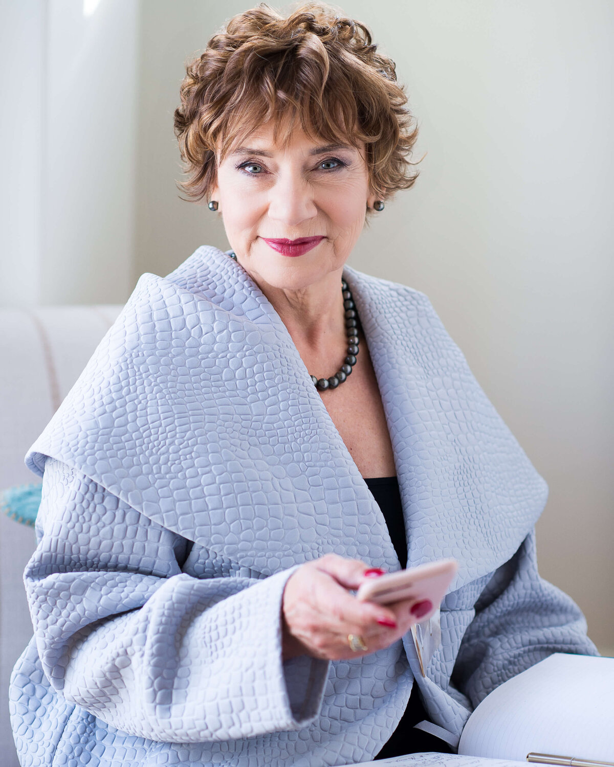 a female realtor in a light blue jacket sitting in a chair holding her cell phone.  Captured indoors by Ottawa Branding Photographer JEMMAN Photography COMMERCIAL